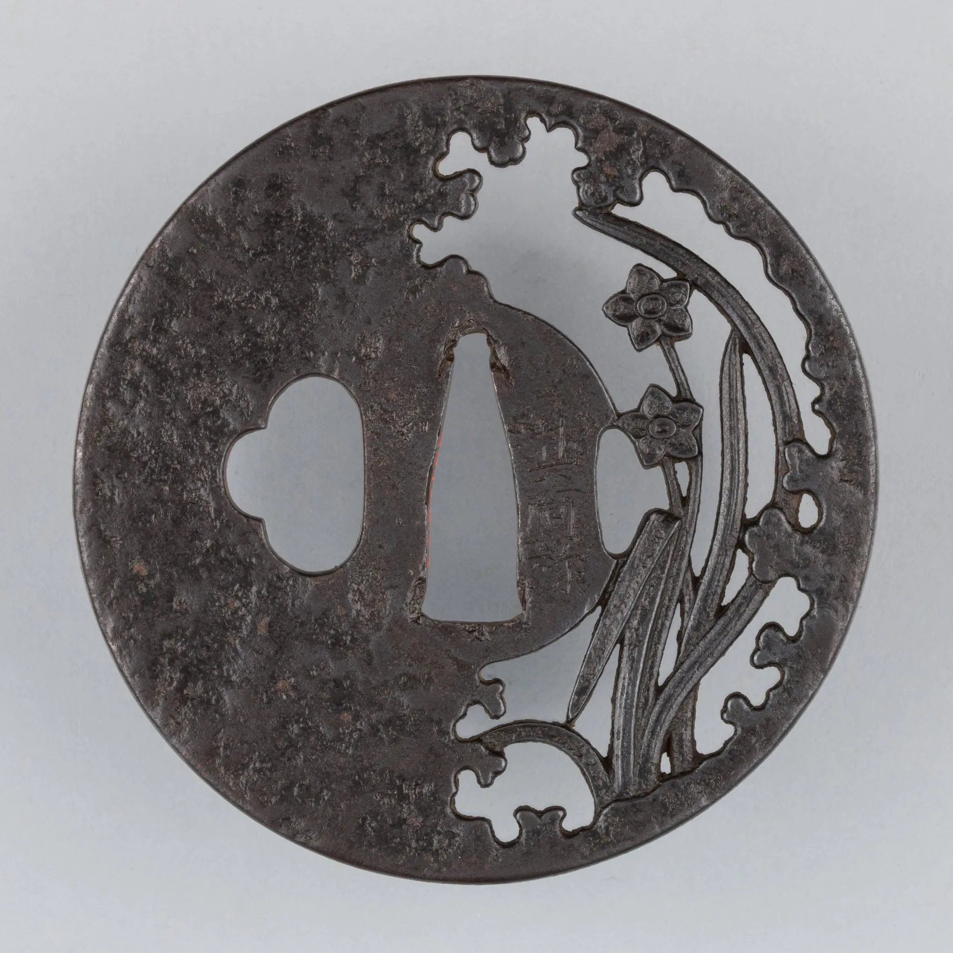Guardamano circular de hierro oscuro con motivos de flores y hojas calados.